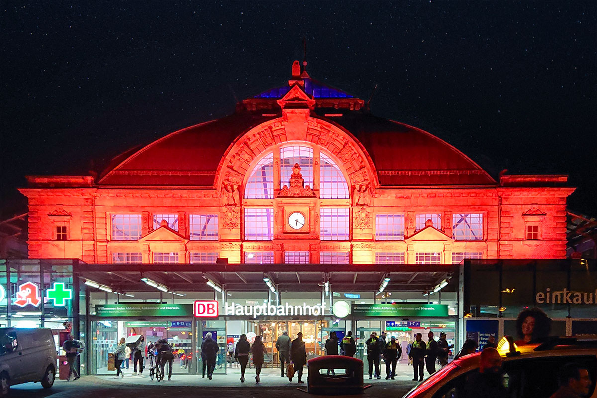 Der Hauptbahnhof Halle wird im dunkeln von außen rot beleuchtet.